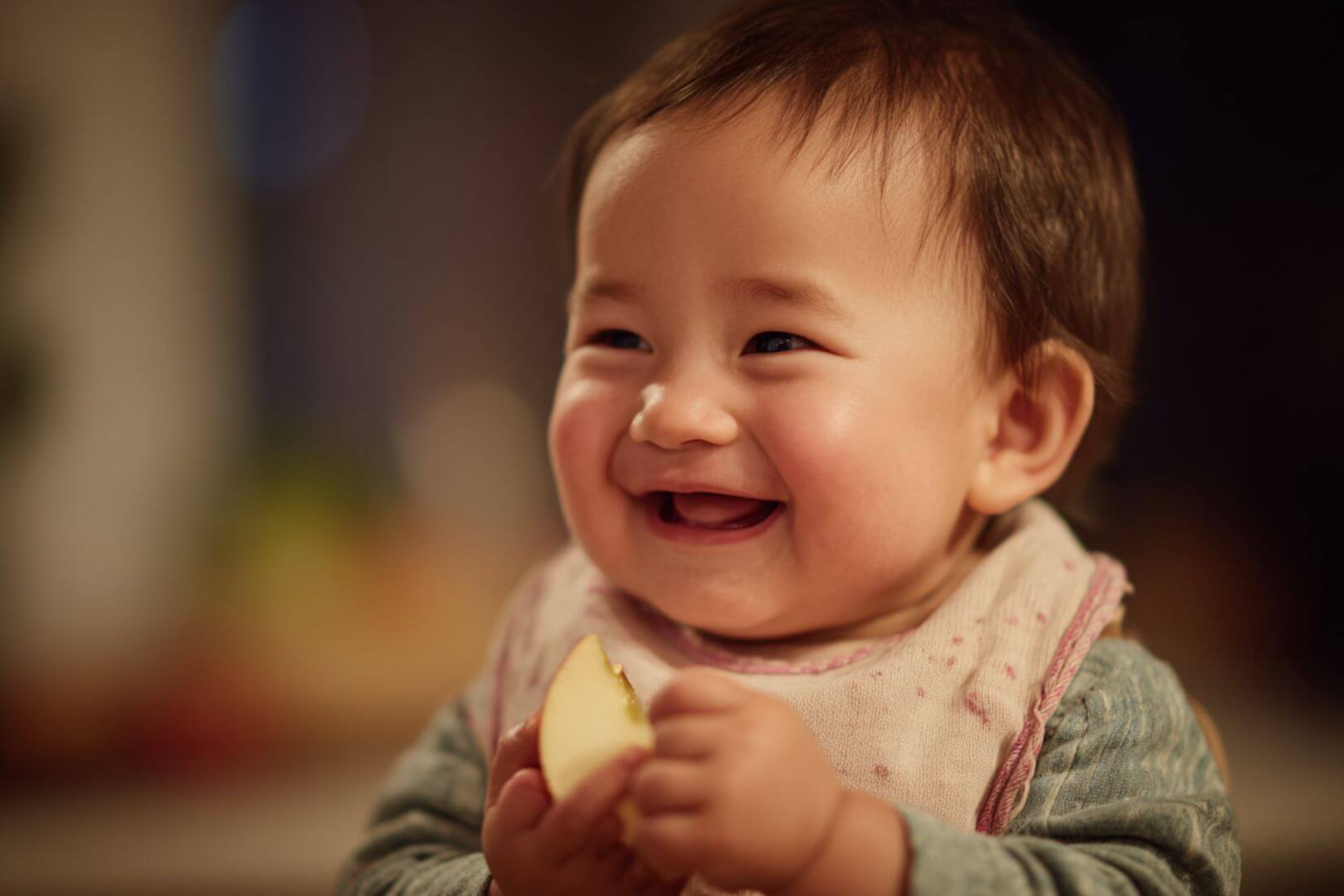 Bebé sonriendo mientras sostiene un trozo de manzana, disfrutando de sus primeras experiencias con el método BLW.