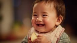 Bebé sonriendo mientras sostiene un trozo de manzana, disfrutando de sus primeras experiencias con el método BLW.