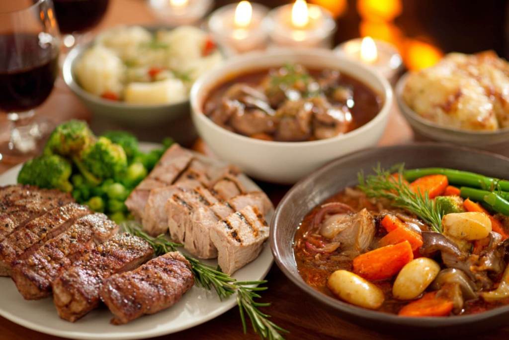 Platos con carne a la plancha, verduras al vapor y estofado casero servidos en una mesa con velas.