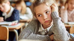 Niña en clase con gesto aburrido, apoyada sobre su mano, mostrando falta de interés durante la lección.