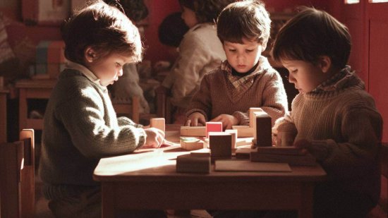 Grupo de niños pequeños en clase Montessori, sentados en una mesa de madera y utilizando bloques para aprender de forma práctica y colaborativa.