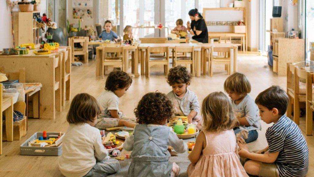 Grupo de niños pequeños en un aula de educación infantil en España, sentados en el suelo y jugando con juguetes de aprendizaje.