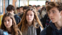 Adolescentes españoles en un pasillo de instituto, con mochilas y expresiones serias.