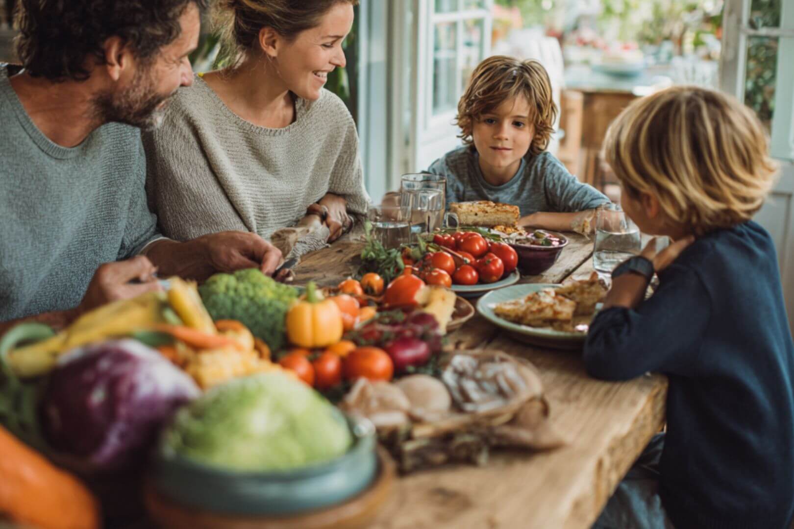 Familia sentada a la mesa disfrutando de una comida saludable con frutas y verduras.
