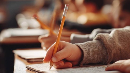 Detalle de manos de niños escribiendo con lápiz en sus cuadernos durante una clase en el colegio