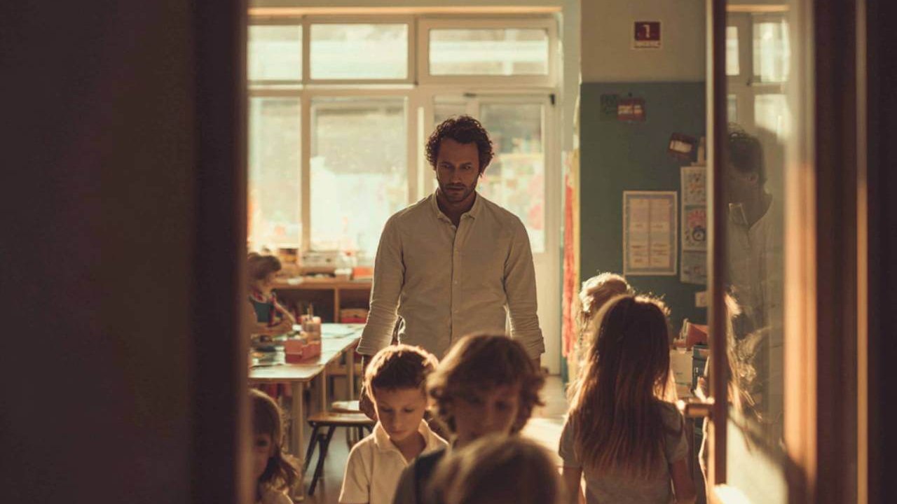 Profesor caminando junto a varios niños que salen de clase en una escuela iluminada por luz natural.