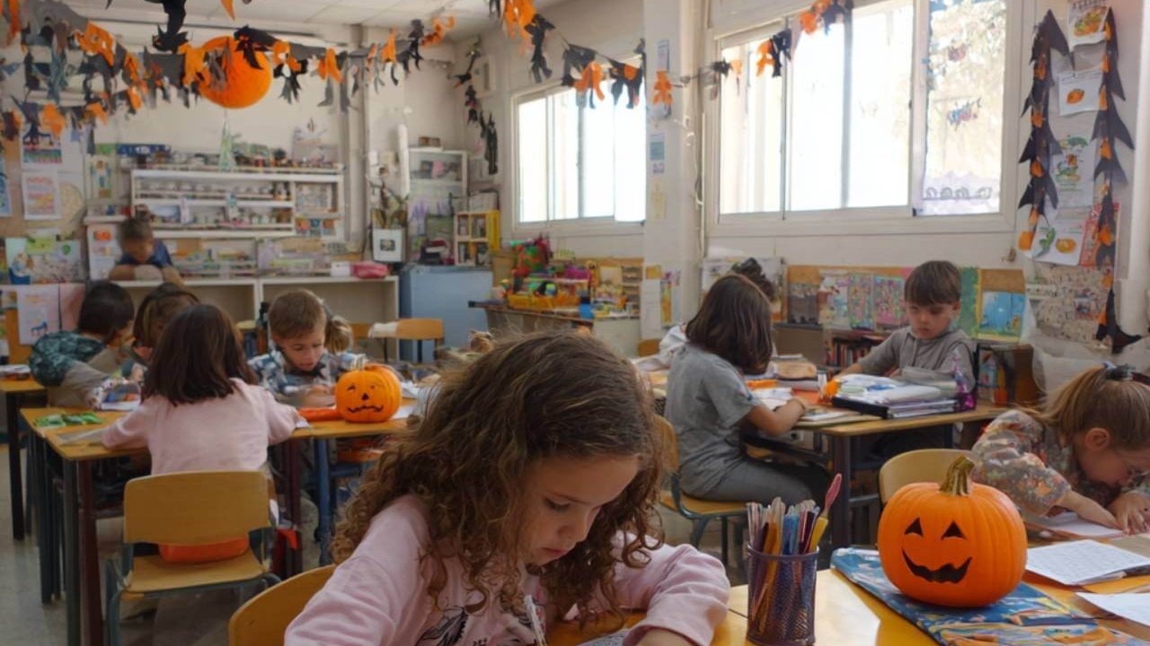 Niños de primaria realizando actividades escolares en un aula decorada con calabazas y adornos de Halloween.
