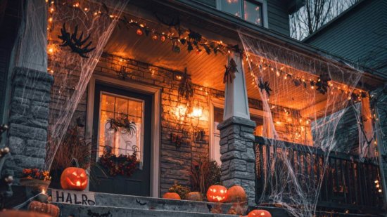 Entrada de casa decorada para Halloween con calabazas iluminadas, velas y carteles con frases divertidas.