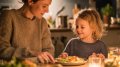 Madre y niño cenando juntos en la cocina, con luz cálida y comida saludable sobre la mesa.