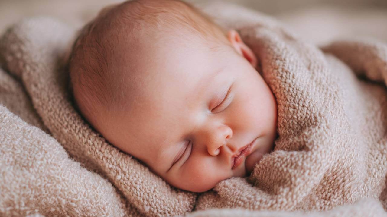 Bebé recién nacido dormido plácidamente, envuelto en una manta de punto color beige.